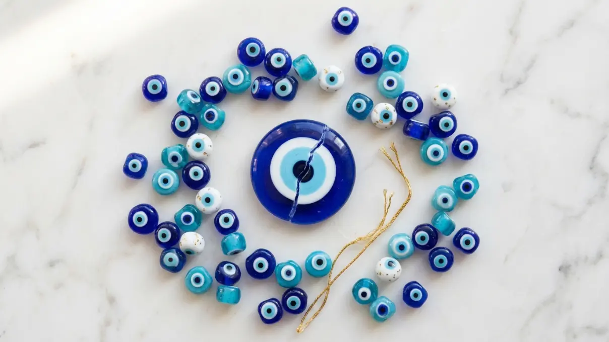 scattered blue evil eye beads and one cracked nazar on a white marble surface with soft natural light, showing different types of bracelet breakage
