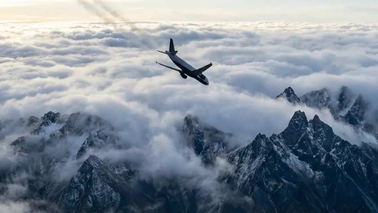 aerial view of rugged mountain peaks breaking through a dense cloud layer with dramatic cold light, sharp contrasts between rock and mist, representing obstacles and crash symbolism in dreams
