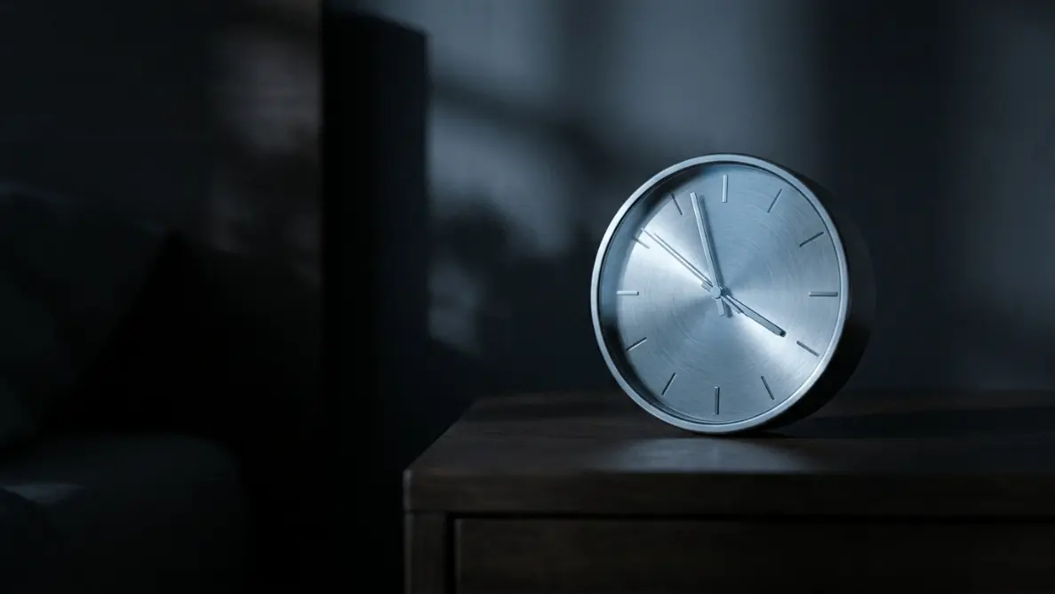 analog clock showing approximately 4 AM on a nightstand in a dark room with faint blue-silver light, representing the spiritual meaning of the early morning hours