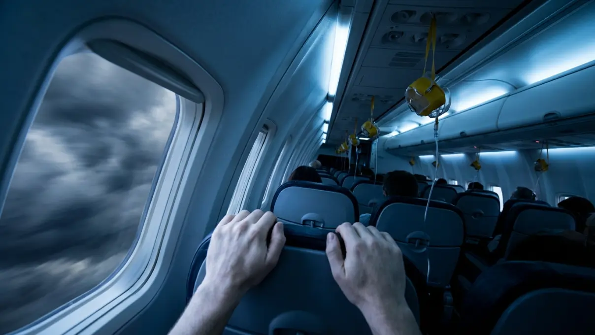 close-up of a person gripping an airplane armrest tightly with white knuckles, dim cabin lighting with cool blue tones, representing anxiety and fear of losing control in a plane crash dream