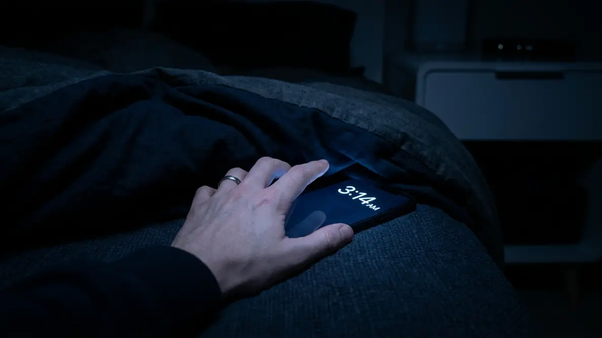 person's hand reaching toward a glowing phone screen showing 3:14 AM in a dark room, cold blue light on fingertips, capturing the moment of waking up at 3am every night
