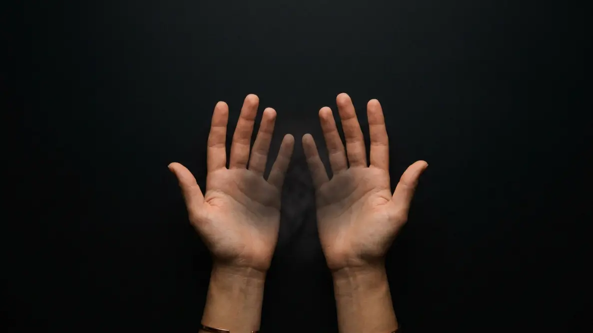 two open hands viewed from above releasing soft light particles against dark background representing emotional release during manifestation