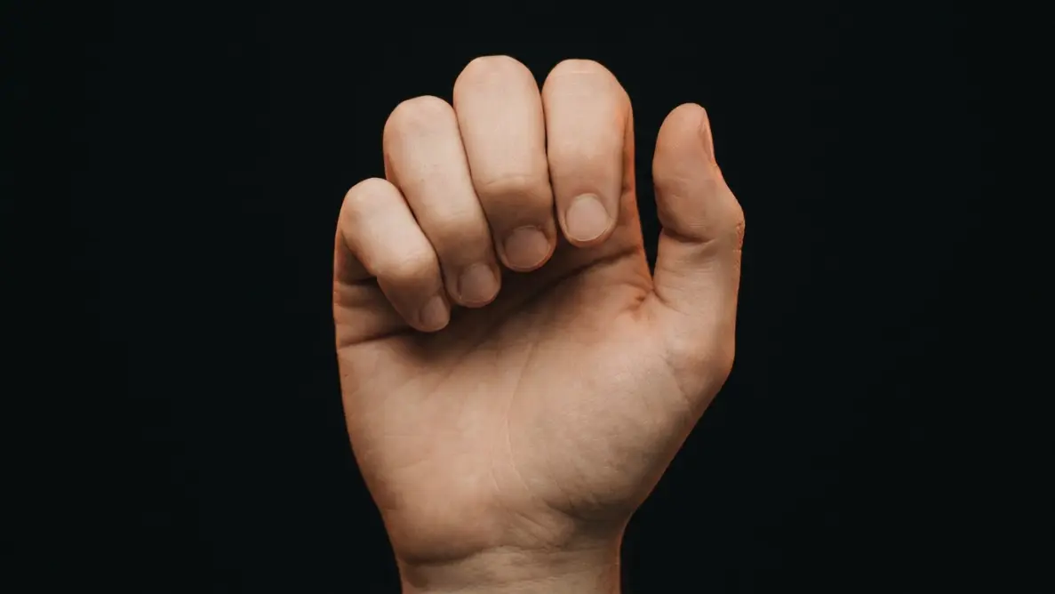 single hand slowly unclenching against muted terracotta background illustrating different forms of letting go