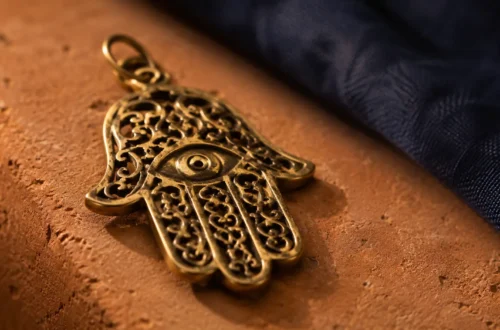 hamsa hand facing up or down meaning — close-up of a golden hamsa amulet on a terracotta surface with warm lighting and indigo background