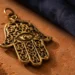 hamsa hand facing up or down meaning — close-up of a golden hamsa amulet on a terracotta surface with warm lighting and indigo background