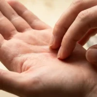 person scratching the center of their left palm with the fingertips of the right hand, illustrating the spiritual meaning of left palm itching linked to money coming in