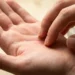 person scratching the center of their left palm with the fingertips of the right hand, illustrating the spiritual meaning of left palm itching linked to money coming in