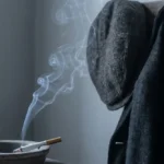 smelling cigarette smoke when no one is smoking, a lit cigarette smoldering in an ashtray beside an old coat and cap in an empty room