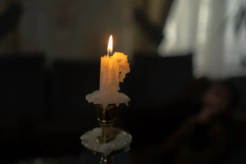 A burning candle with melted wax running down one side and pooling unevenly at its base
