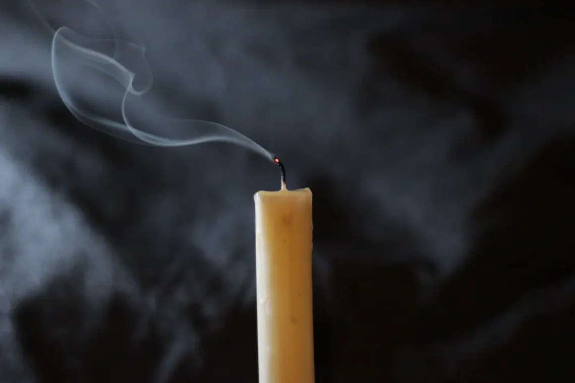 A candle with a smoking wick moments after the flame stopped, against a dark background