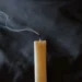 A candle with a smoking wick moments after the flame stopped, against a dark background