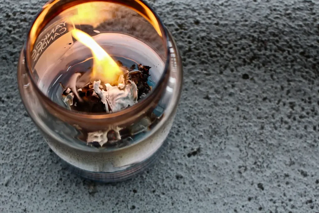 A container candle burning with liquid wax reaching the edge of the glass