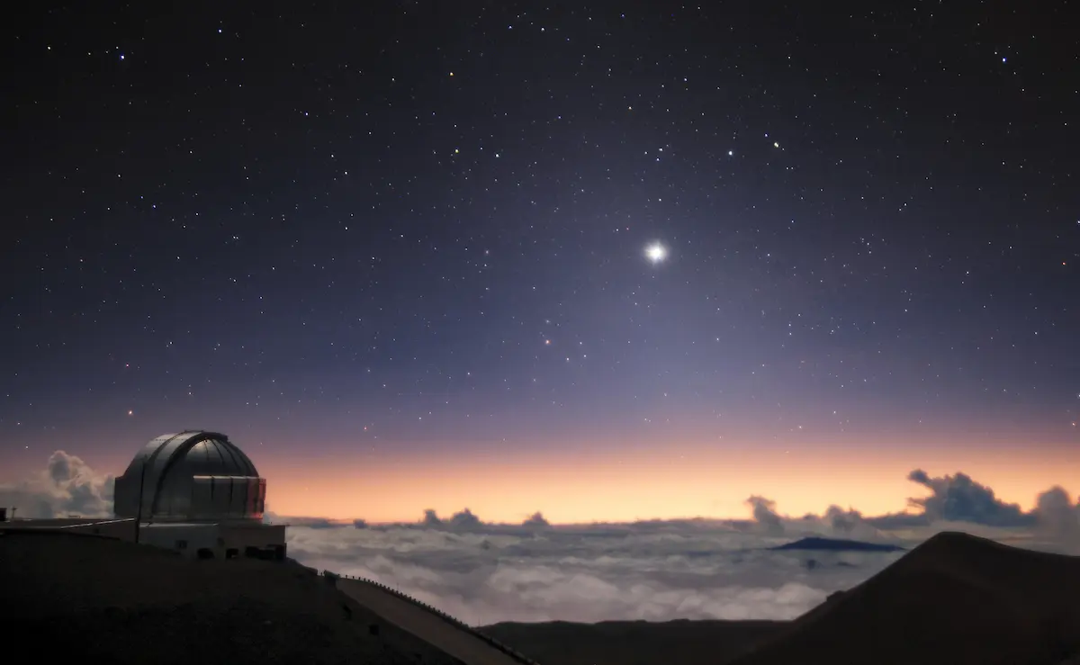 Jupiter and Saturn shining as a single bright point above an observatory dome and a sea of clouds at dusk